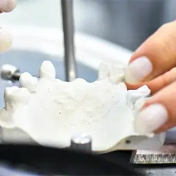 Modelo dentário sendo ajustado com instrumento em bancada de trabalho